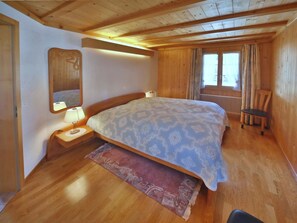 A bedroom with a bed, nightstands, a mirror, a window with curtains, and a radiator. - Hohliebestrasse 24 Appartement/Fewo, Dusche und Bad, WC, 2 Schlafräume by Interhome (Lenk)