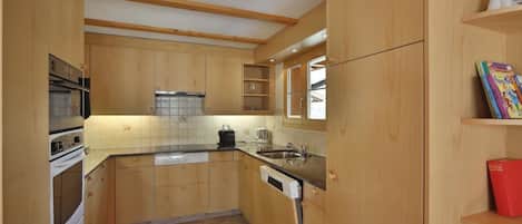A compact kitchen with wooden cabinets, a built-in oven, a dishwasher, and a window above the sink.