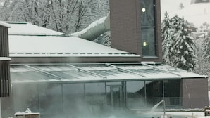 Un bâtiment doté d’une piscine intérieure à parois de verre, entourée de neige.