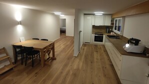 Une cuisine compacte avec des meubles blancs, une table à manger en bois et un four encastré.