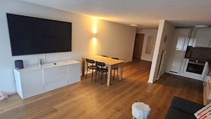 Un appartement moderne comprenant un coin repas, une cuisine, un salon avec un canapé et un téléviseur fixé au mur.