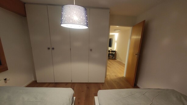 Une chambre avec deux lits, une armoire, un luminaire suspendu et une vue sur la salle à manger.