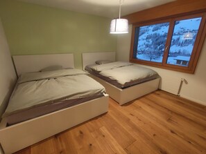 Un dormitorio con dos camas, una ventana que ofrece vistas a un paisaje nevado y una lámpara colgante.