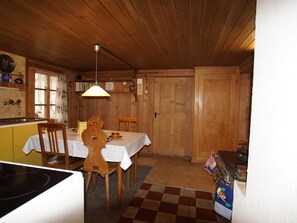 Ein Holzinterieur mit Esstisch, Stühlen, einer Küchenzeile und einem Schachbrettfußboden.