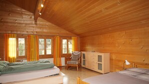 Een houten chalet met twee bedden, een stoel, een dressoir en een raam met gordijnen.