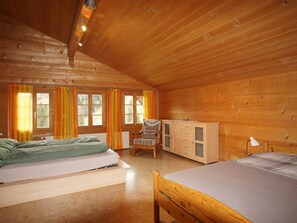 Eine Holzhütte mit zwei Betten, einem Sessel, einer Kommode und einem Fenster mit Vorhängen.