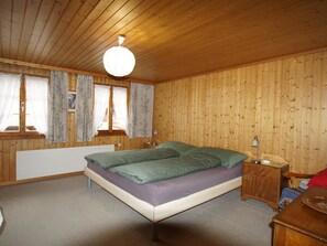 Ein Zimmer mit Holzwänden, einem Bett, einem Nachttisch und einem Fenster mit Vorhängen.