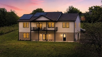 A two-story house with a balcony, solar panels, and a well-lit entrance.
