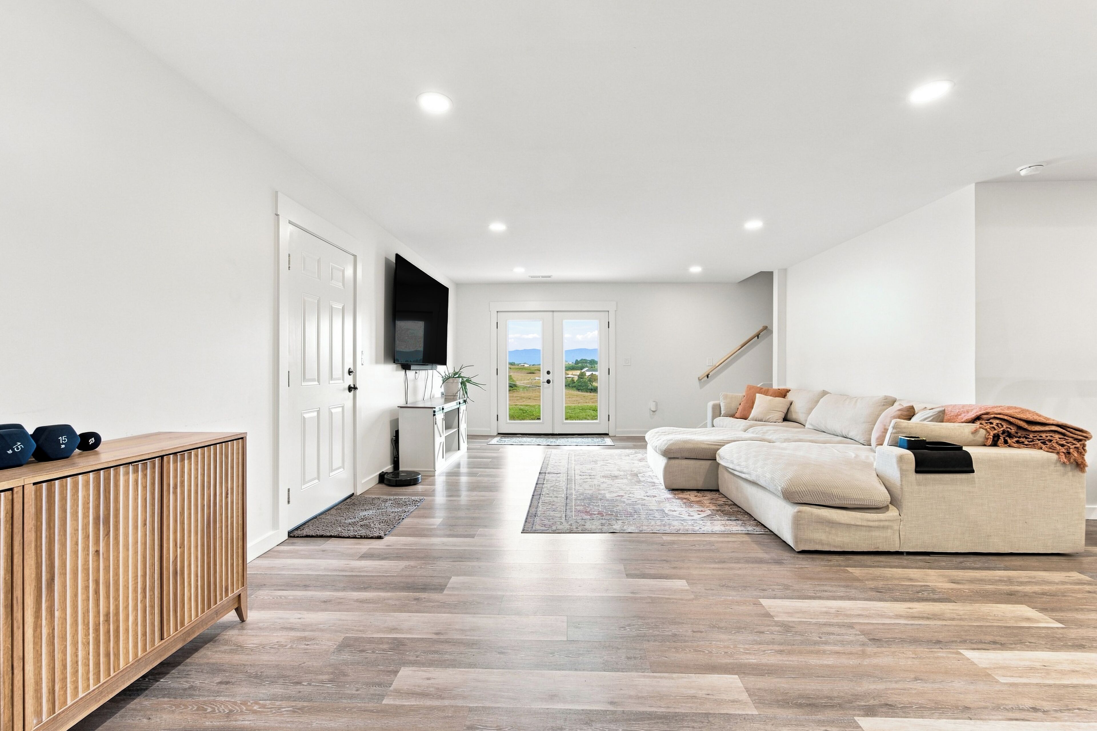 Un salon moderne avec un canapé, un téléviseur et une vue sur l’extérieur, visible à travers une porte vitrée.