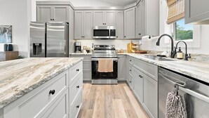 Una cocina moderna con armarios grises, electrodomésticos de acero inoxidable, encimera de mármol y suelo de madera.