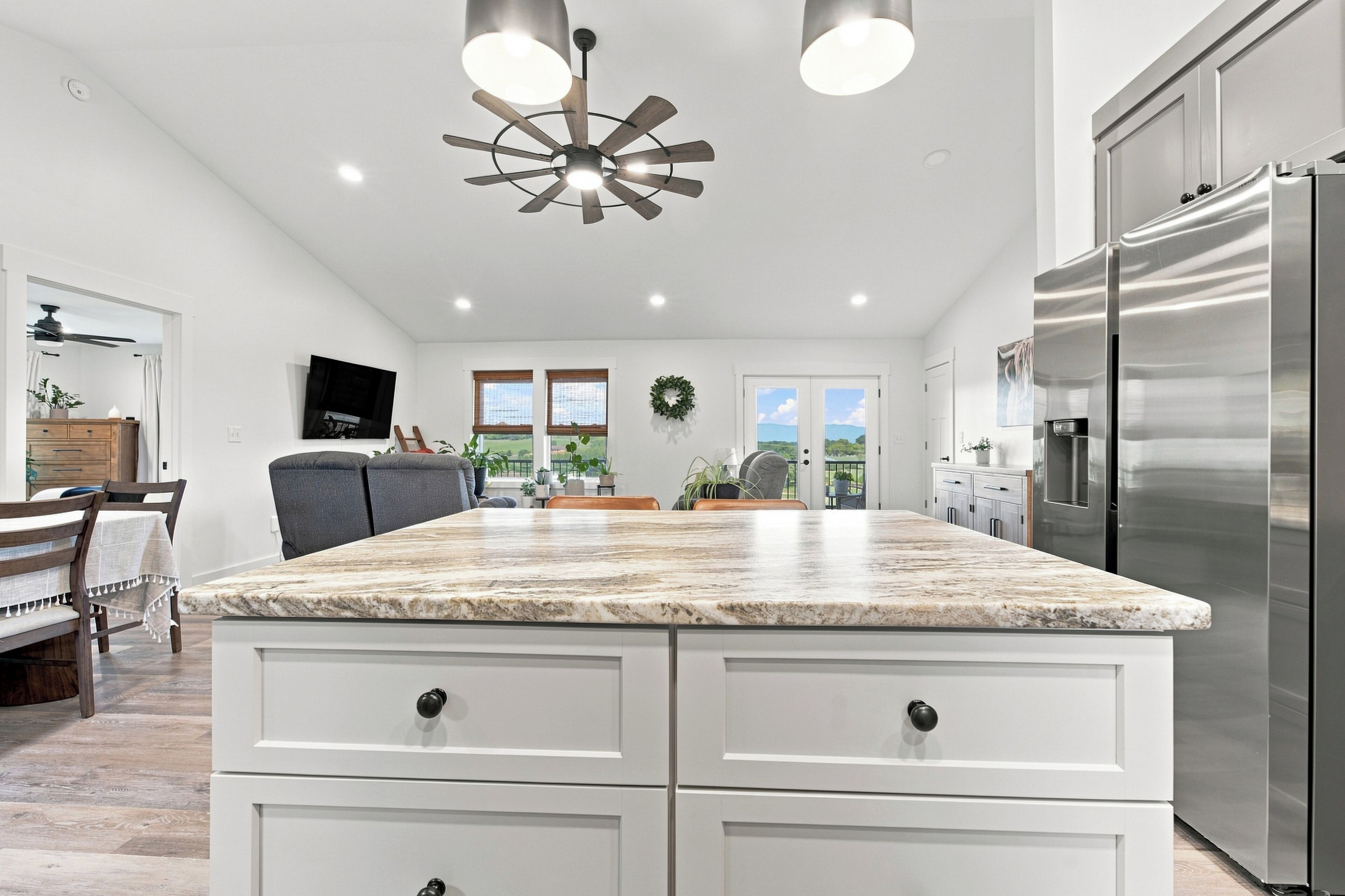 A modern kitchen with a large island, stainless steel appliances, and a ceiling fan.