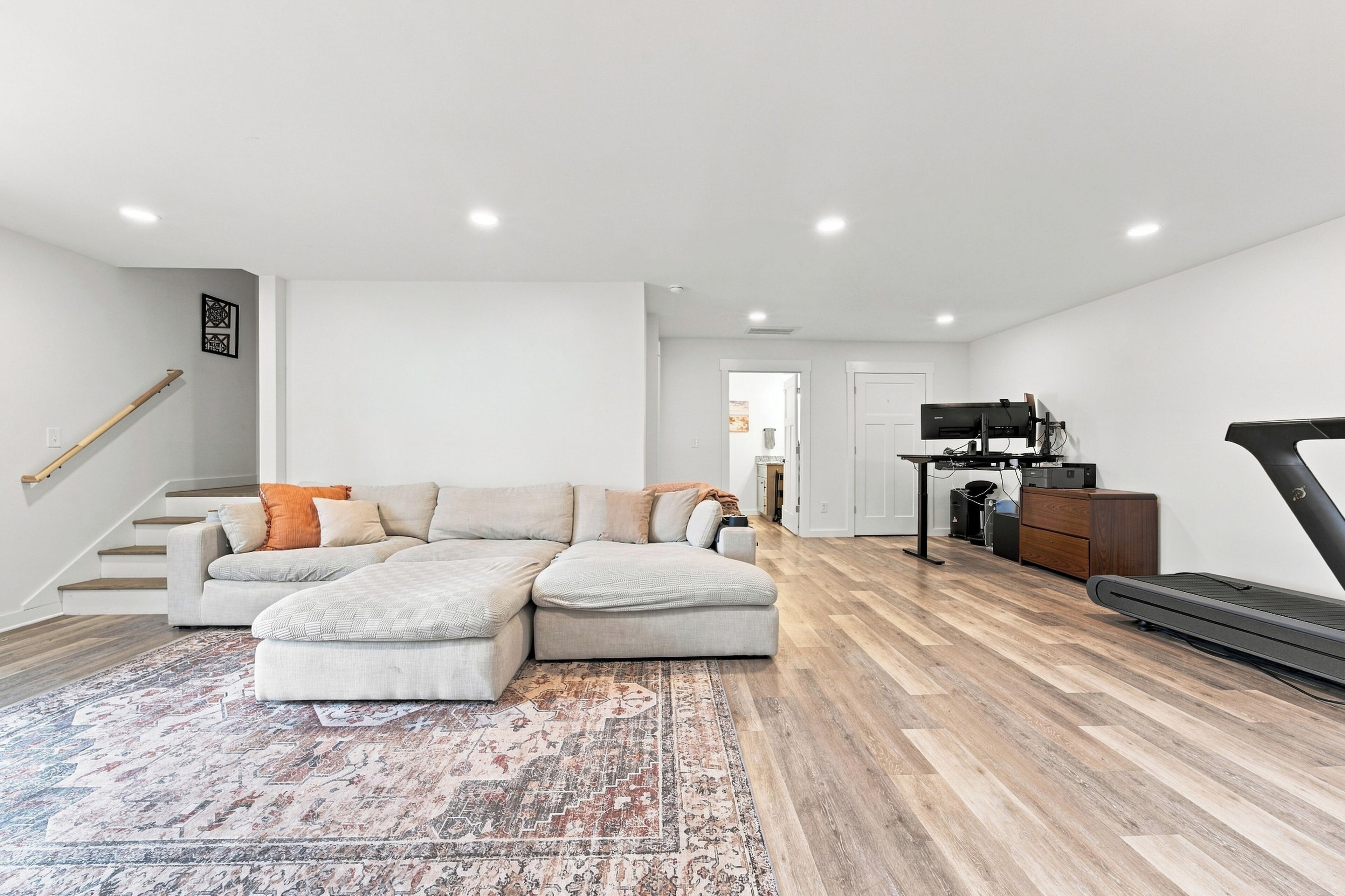 Una sala de estar moderna con un sofá modular, una cinta de correr y un televisor de pantalla plana.