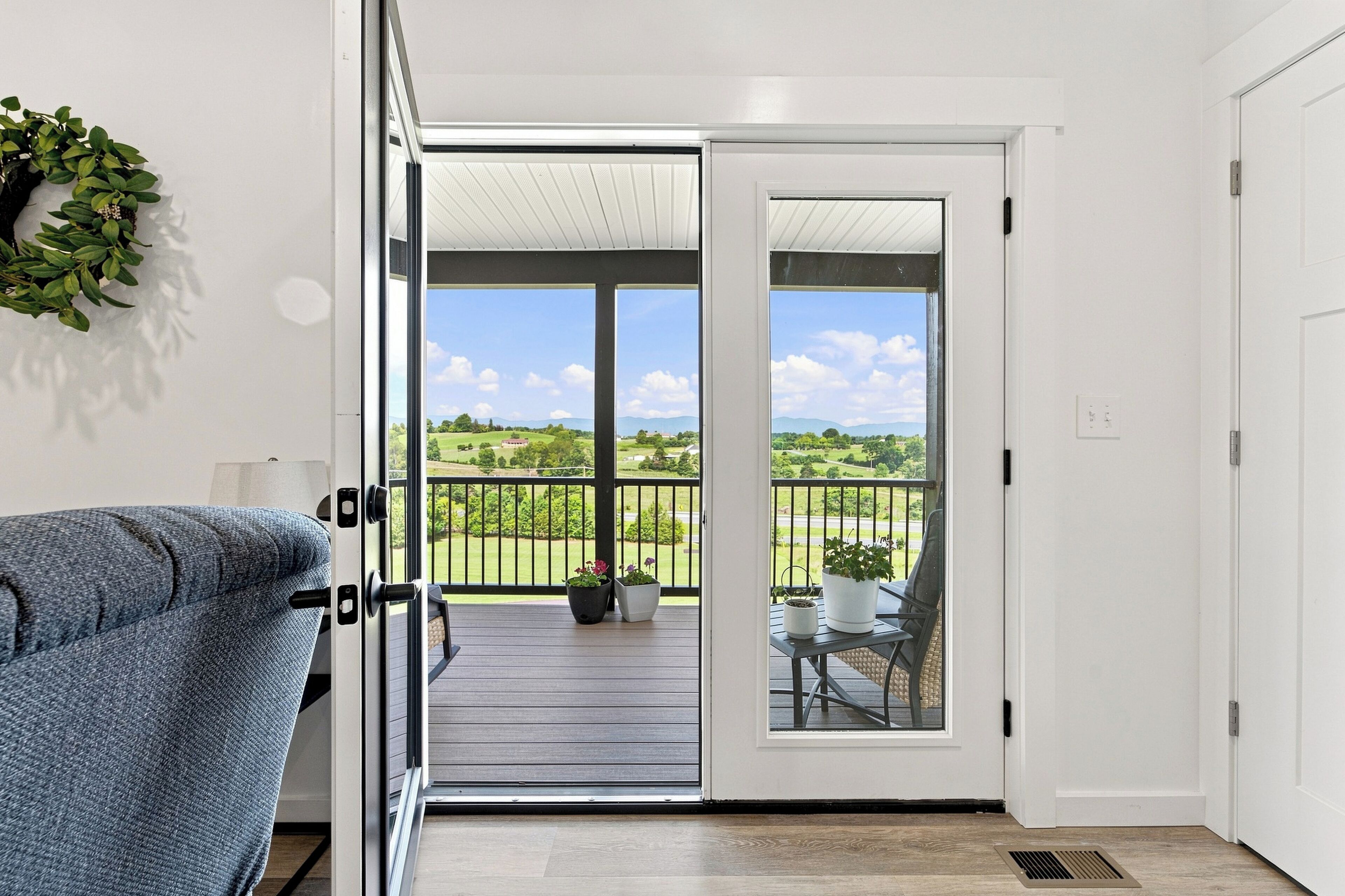An open door leading to a balcony with a view of a green landscape and a clear sky.