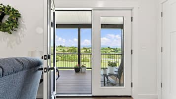 An open door leading to a balcony with a view of a green landscape and a clear sky.