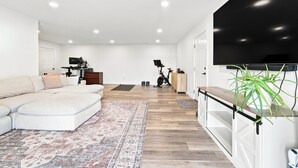 Una sala moderna con sofá, alfombra, televisión y equipo de ejercicio.
