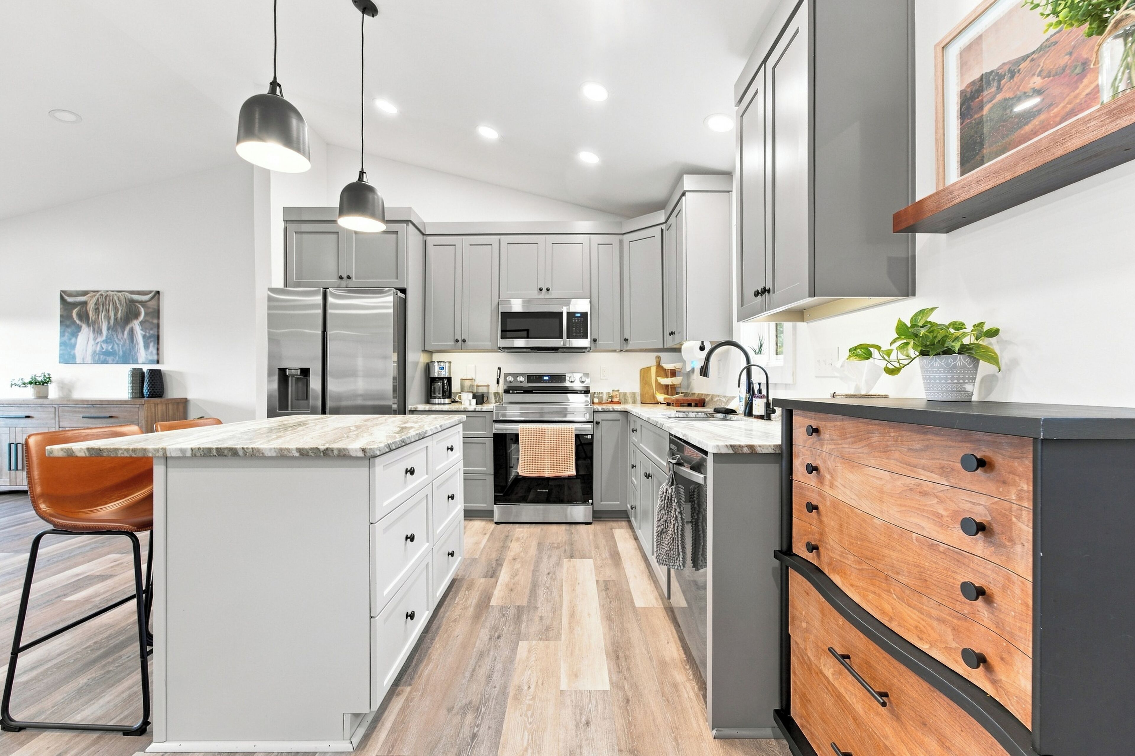 A modern kitchen with grey cabinets, stainless steel appliances, a marble countertop, and a wooden island with drawers.