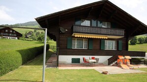 A wooden chalet with a balcony, a small patio with outdoor seating, and a view of a green landscape. - Béatrice Appartement/Fewo, Dusche oder Bad, WC, 2 Schlafräume 4-Bett-Wohnung by Interhome (Lenk)