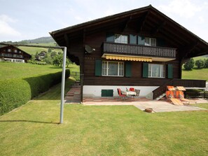 Eine Holzhütte mit einem Balkon, einer kleinen Terrasse mit Sitzgelegenheit und Blick auf eine grüne Landschaft.