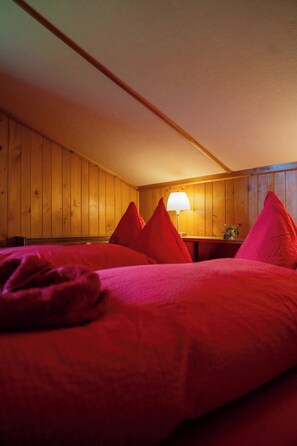 A room with wooden panel walls, a bed with red bedding, and a lamp on a bedside table. - Béatrice Appartement/Fewo, Dusche oder Bad, WC, 2 Schlafräume 4-Bett-Wohnung by Interhome (Lenk)