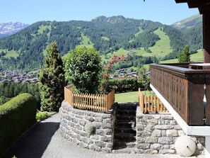 Eine Steintreppe führt zu einer Holzdar Terrasse mit Blick auf ein Dorf und Berge.