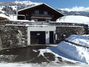 Eine Berglodge mit steinverkleideter Fassade, einem Holzbalkon und Blick auf verschneite Berge.