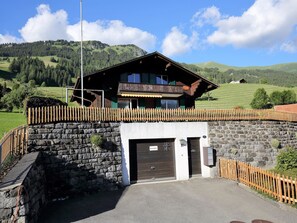 Un chalet avec une entrée en pierre, une clôture en bois et une vue sur les montagnes en arrière-plan.