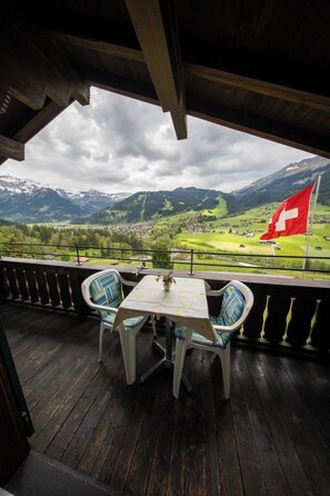 A balcony with a table and chairs, overlooking a village and mountains, with a Swiss flag visible. - Béatrice Appartement/Fewo, Dusche oder Bad, WC, 2 Schlafräume 4-Bett-Wohnung by Interhome (Lenk)