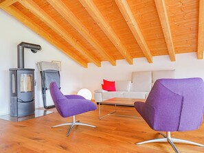 A modern living room with a high wooden ceiling, a wood-burning stove, two purple chairs, a white sofa with red cushions, and a wooden coffee table. - Kronenplatz 11 OG Appartement/Fewo, Bad, WC, 2 Schlafräume 4 Bettwohnung by Interhome (Lenk)
