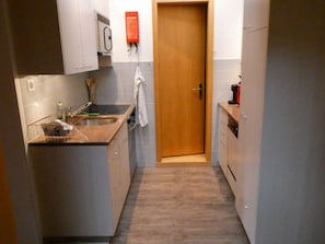 A compact kitchen with a sink, cabinets, and a door leading to another room. - Chalet Waldchutz - Wohnung Anax Appartement/Fewo, Dusche, WC, 2 Schlafräume by Interhome (Lenk)