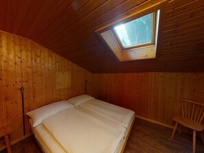 Ein Zimmer mit schrägen Wänden, einem Oberlicht, einem Bett und einem Sessel.