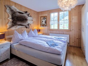 Ein Schlafzimmer mit einem großen Bett, Holzwänden, einem aufgehängten Fellkopf und einem Fenster mit Blick auf eine verschneite Landschaft.