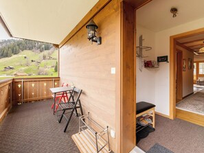 Interior de fusta amb taula i cadires, vista a un paisatge verd, i una porta que dona a una altra habitació.