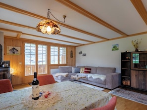 Ein gemütliches Wohnzimmer mit einer Couch, einem Esstisch mit einer Flasche und einer Holzzieldecke.
