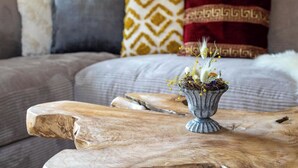 Ein Holztisch mit einem Blumenstrauß im Vordergrund, eine graue Couch mit gemusterten Kissen im Hintergrund und eine Holzvertäfelung an der Wand.