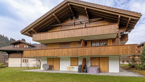 Eine zweistöckige Holzhütte mit Balkon, überdachter Veranda und kleiner Sitzgruppe im Freien.