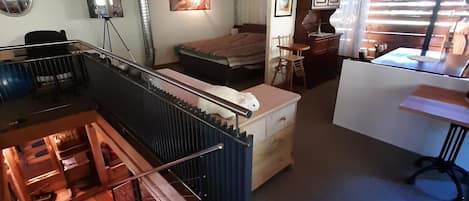 Une pièce de style « loft », avec un plafond haut, un lit, un bureau et un escalier.