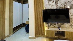 A modern hotel room with a flat-screen TV mounted on a wooden panel, a large mirror, and a bed with a white bedspread.