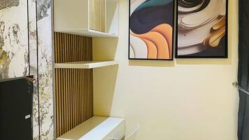 A modern hotel room with a white desk, a chair, a bed, and two abstract paintings on the wall.