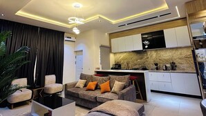 Una sala moderna con un sofá, un reposapiés y una zona de comedor con una cocina al fondo.