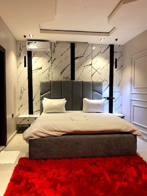 Un dormitorio moderno con una cama grande, paredes con diseño de mármol y una alfombra roja y mullida.