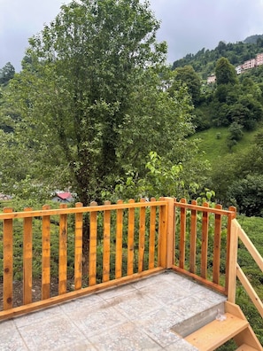 Una escalera de madera que conduce a una terraza con vistas a una colina verde y exuberante y un árbol.