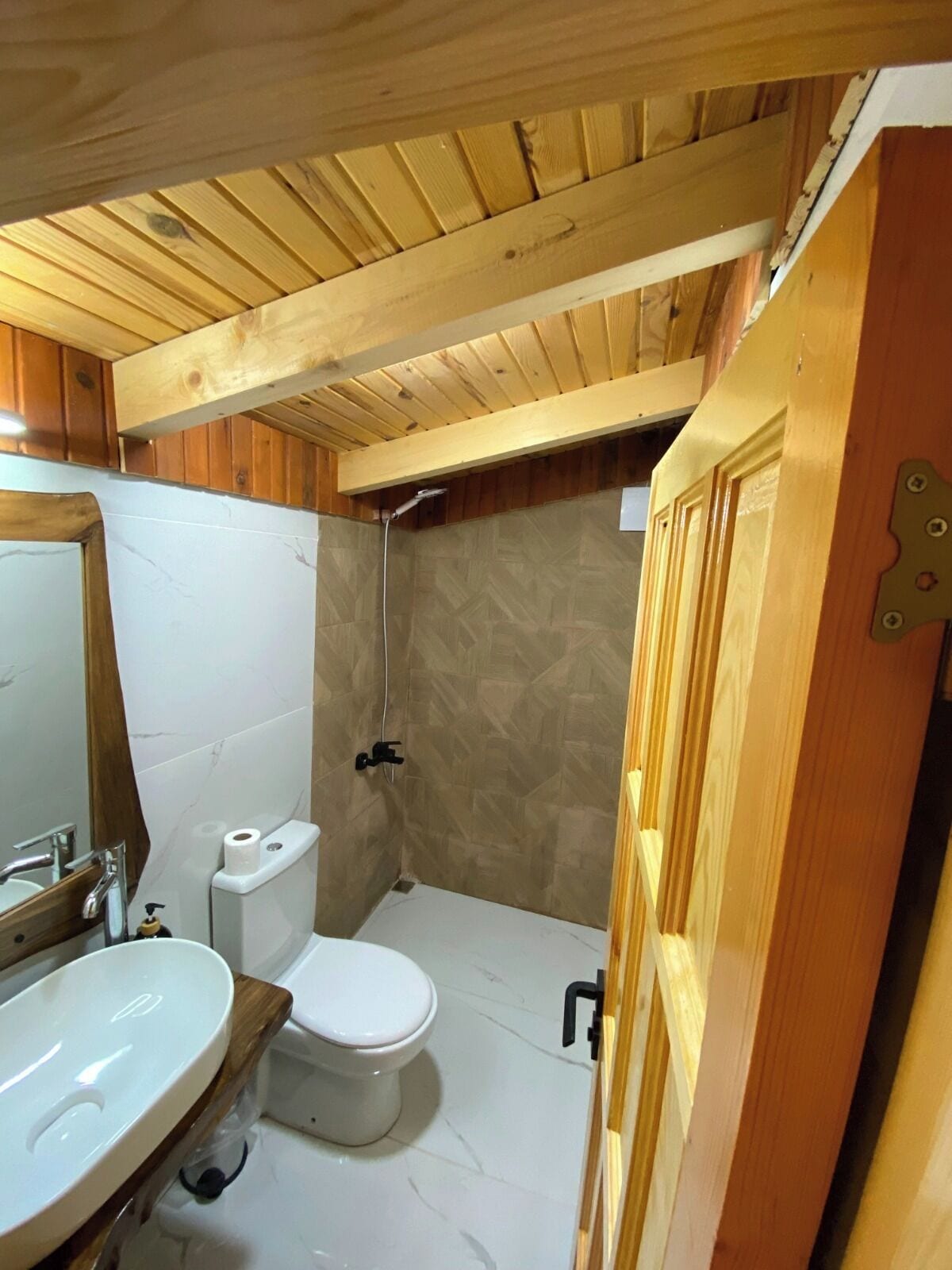 Une petite salle de bain avec un plafond en bois, des toilettes blanches, un lavabo et un espace douche.