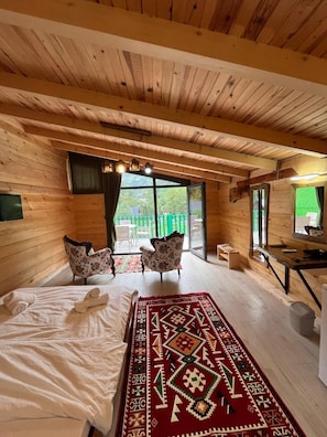 A wooden cabin room with a bed, two chairs, a desk, and a large window. - Lelvani Suit Bungalow (Çamlıhemşin)