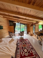 Una habitación tipo cabaña de madera con una cama, dos sillas, un escritorio y un ventanal grande.