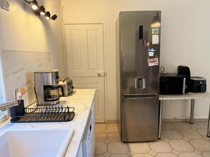 Eine kleine Küche mit einem Edelstahl-Kühlschrank, einer Kaffeemaschine, einem Toaster und einer Mikrowelle auf einer Arbeitsfläche.