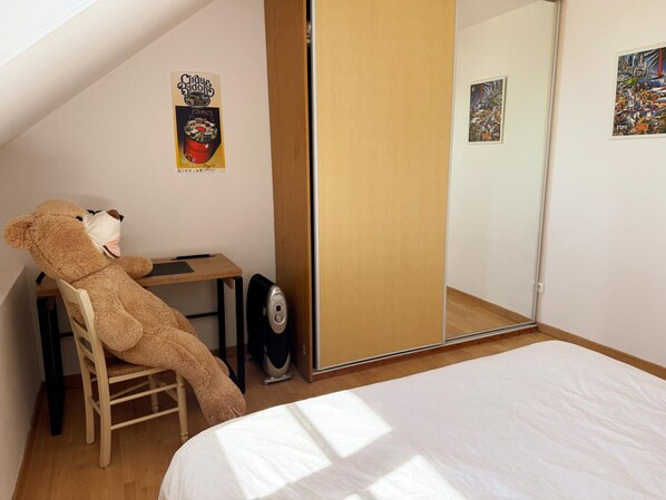 Ein Schlafzimmer mit Bett, Stuhl, Schreibtisch, Teddybär, Spiegel und Tür.