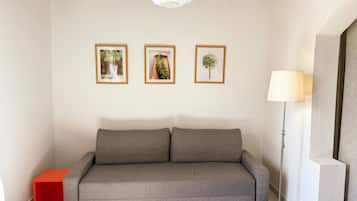 A neutral-toned room with a grey sofa, a small red side table, and a floor lamp.
