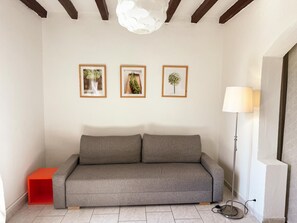 Ein farblich neutrales Zimmer mit einem grauen Sofa, einem kleinen roten Beistelltisch und einer Stehlampe.