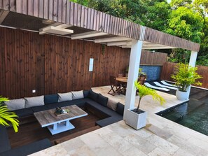 A modern outdoor patio with a wooden wall, seating, a dining table, and a pool. - Villa panoramic view, air conditioning - 8 guests (Saint-Philippe)