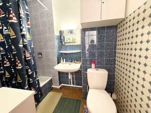 A bathroom with a bathtub, sink, toilet, and shower curtain with sailboat patterns. - T2 apartment sea view - 4 guests (Le Barcarès)